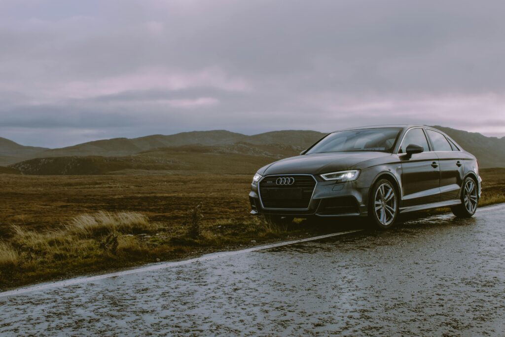 pexels-photo-1719648-1719648 A luxury Audi sedan parked on a wet mountain road with moody skies and a scenic backdrop.